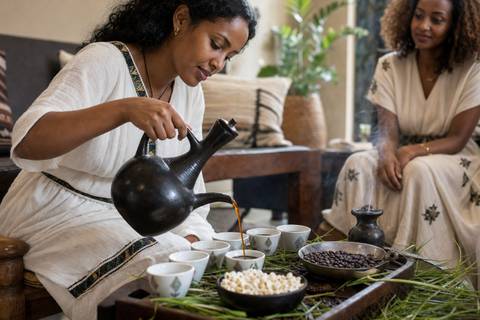 An Ethiopian woman pouring coffee from a black jebena during a home coffee ceremony