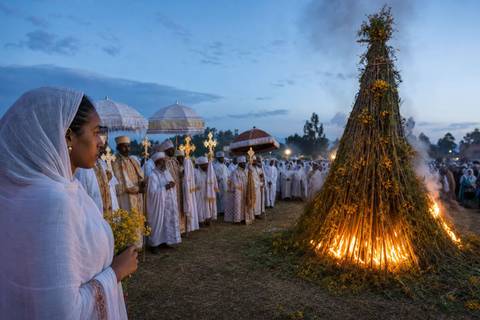Meskel celebration with a tall Demera bonfire, Ethiopian Orthodox clergy, and worshippers carrying yellow flowers
